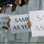 Row of people all wearing white clothes. They are all holding signs that say "Same as you" - this is a largely decorative image meant to invoke that sometimes groups of people can be homogenous